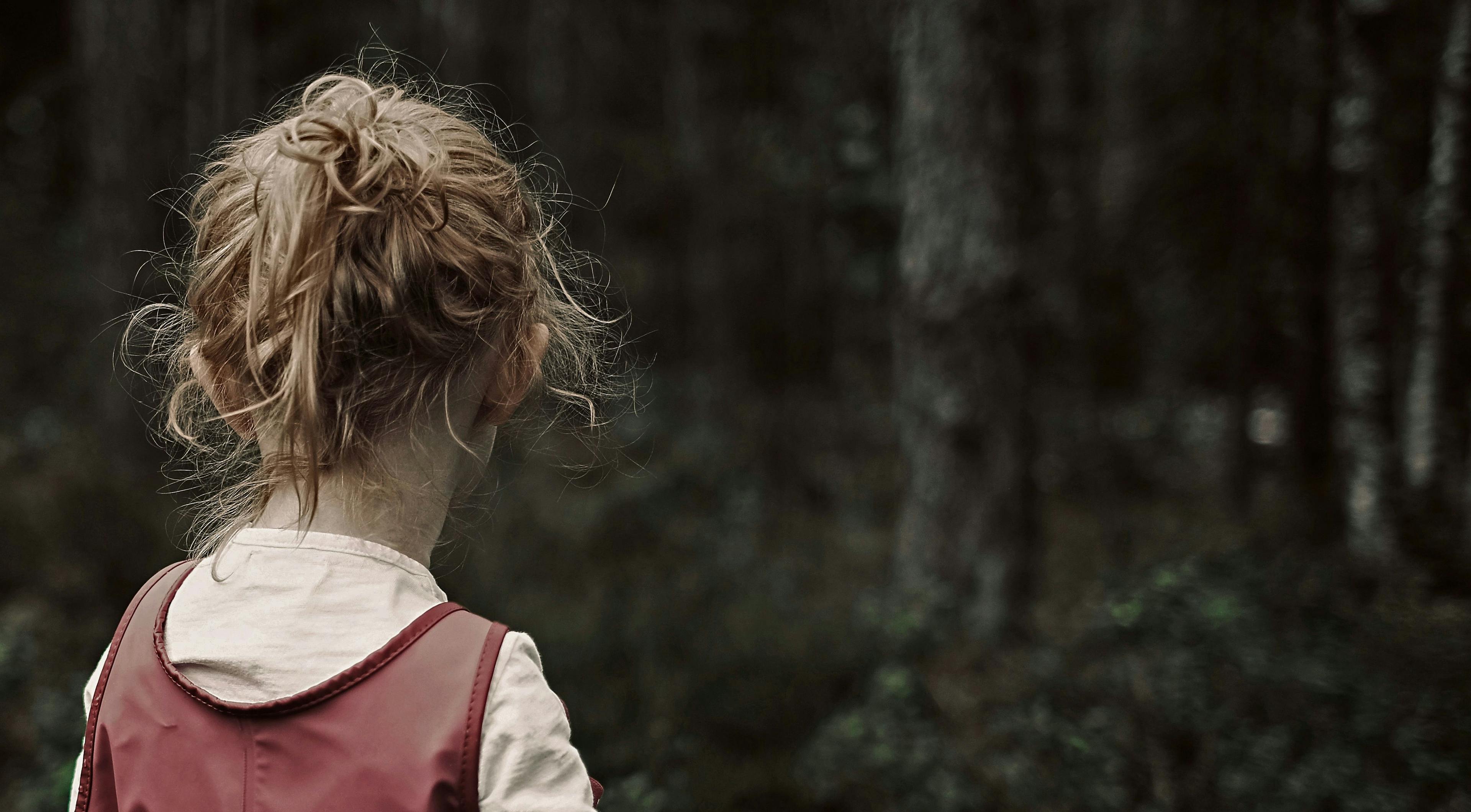 Bilde av et lite barn i skogen som står med ryggen til