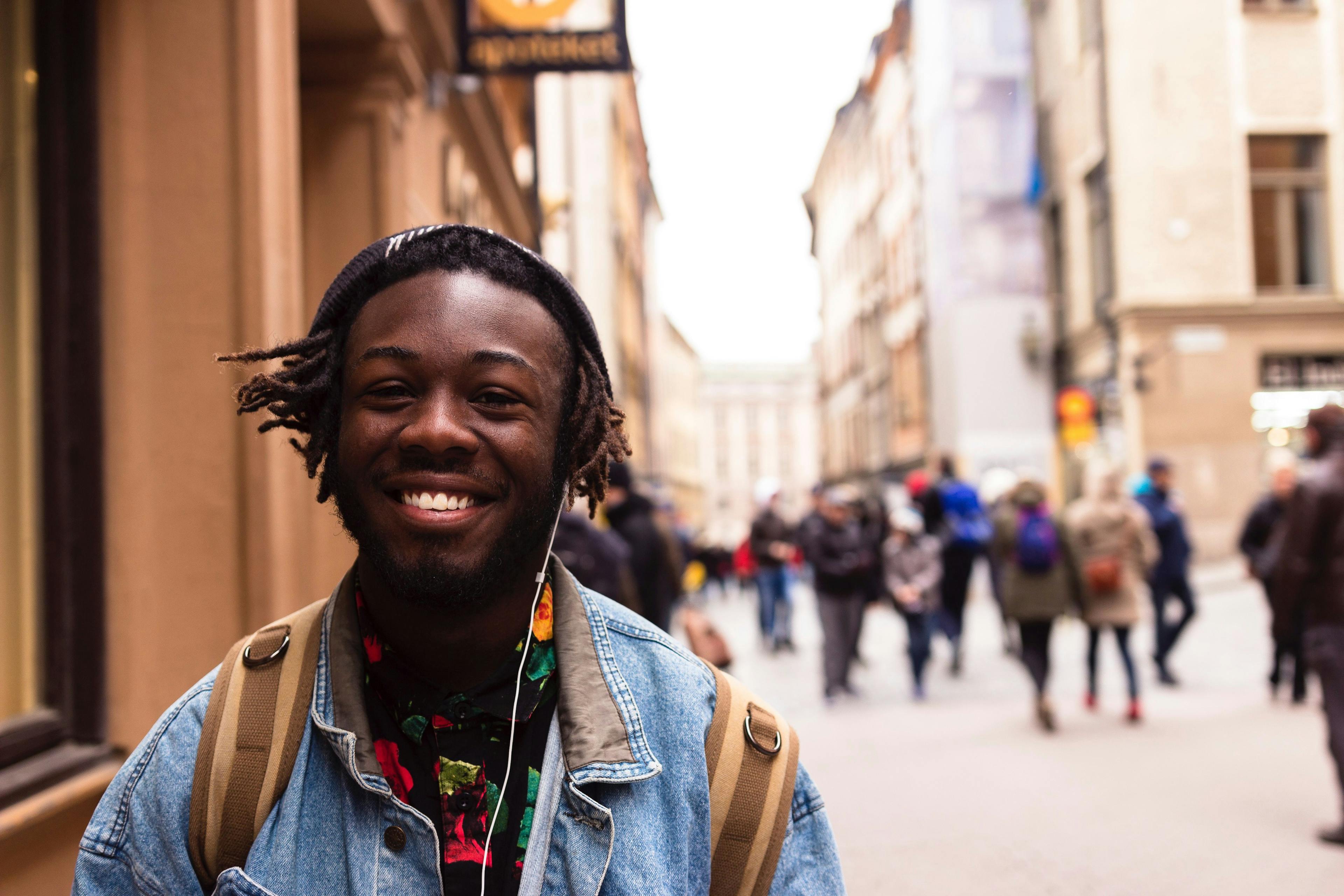 Ung mann som smiler i gata med hodetelefoner i ørene.