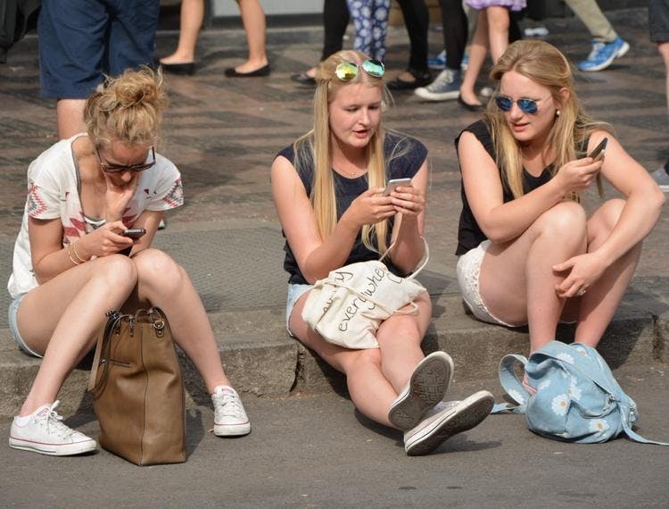 Bilde av tre unge kvinner som sitter og ser i mobilen sin på en fin sommerdag